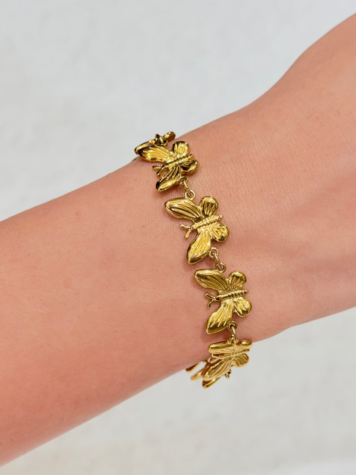 A gold-tone bracelet featuring five detailed butterfly charms linked together, shown worn on a person's wrist against a light gray background.